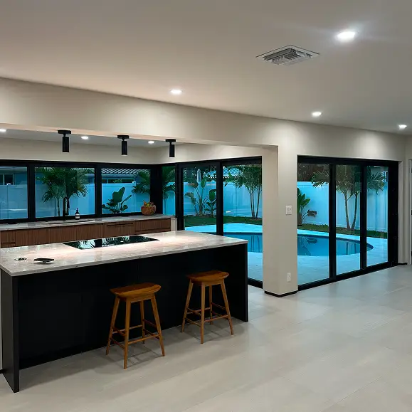 Modern open-concept kitchen remodeling with a large black island overlooking a custom backyard pool.